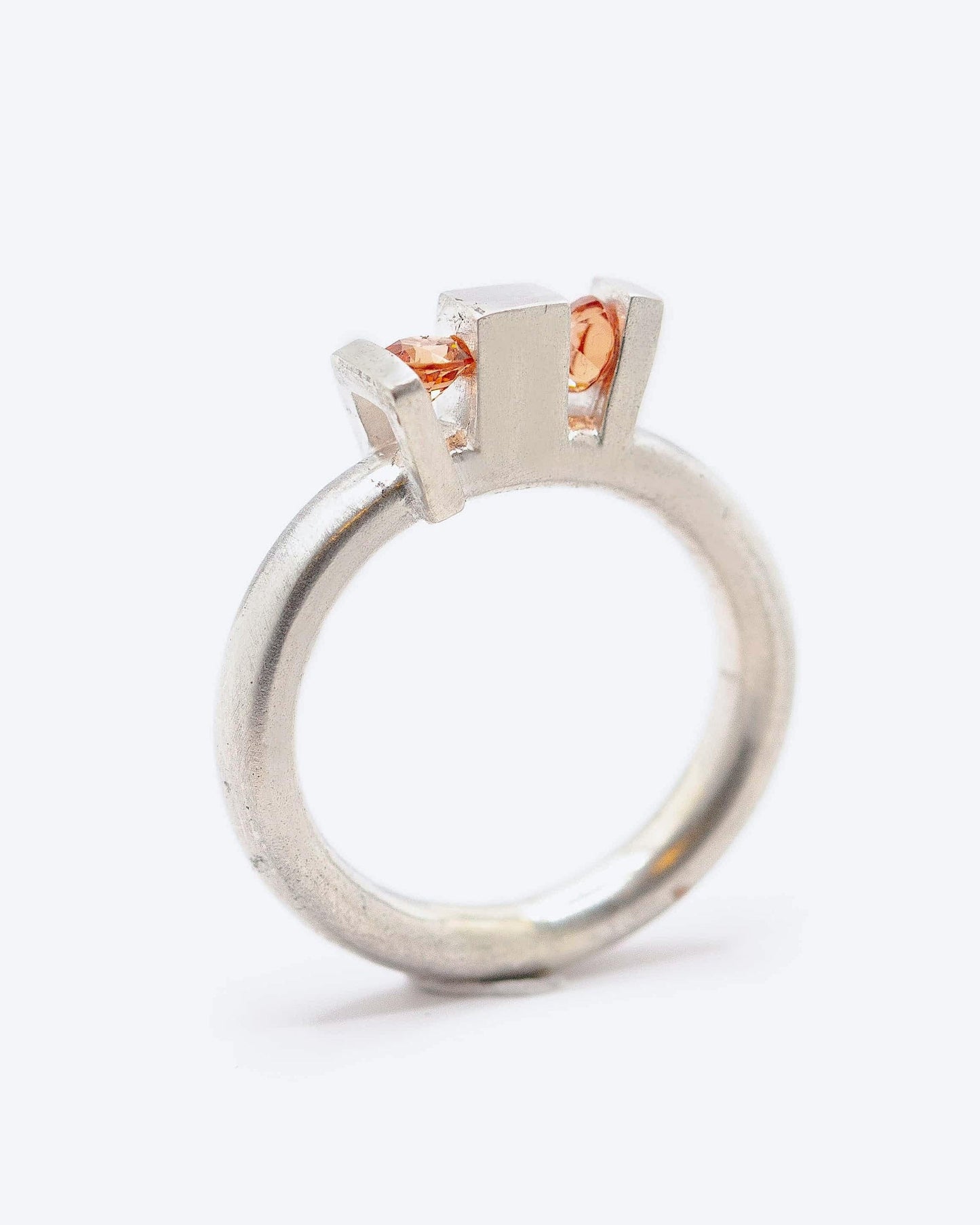 Bague géométrique Skyline en argent avec anneau rond et volumes architecturaux, sertie de deux grenats spessartite aux teintes orange lumineuses.