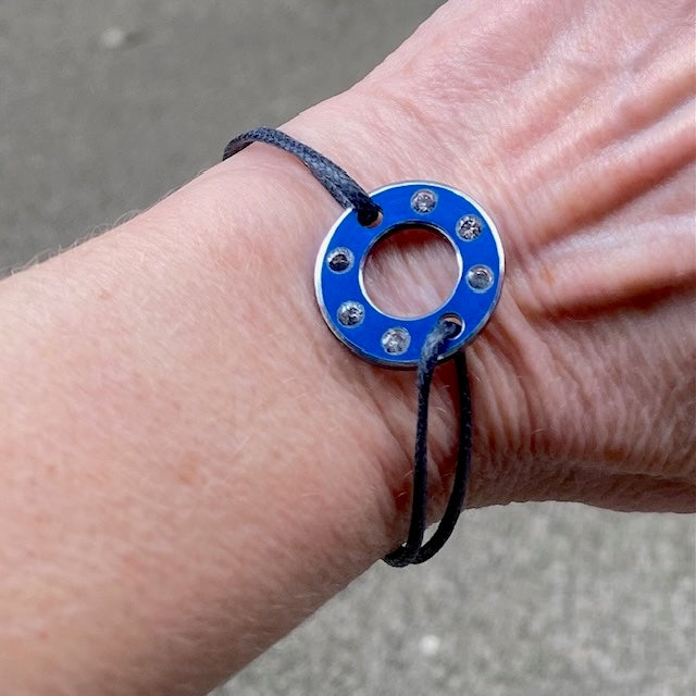 Bracelet Ready-Made, rondelle en aluminium bleu et six saphirs blancs. bijou upcyclé inspiration moto, présenté sur lien de coton réglable. Détail, bijou porté.