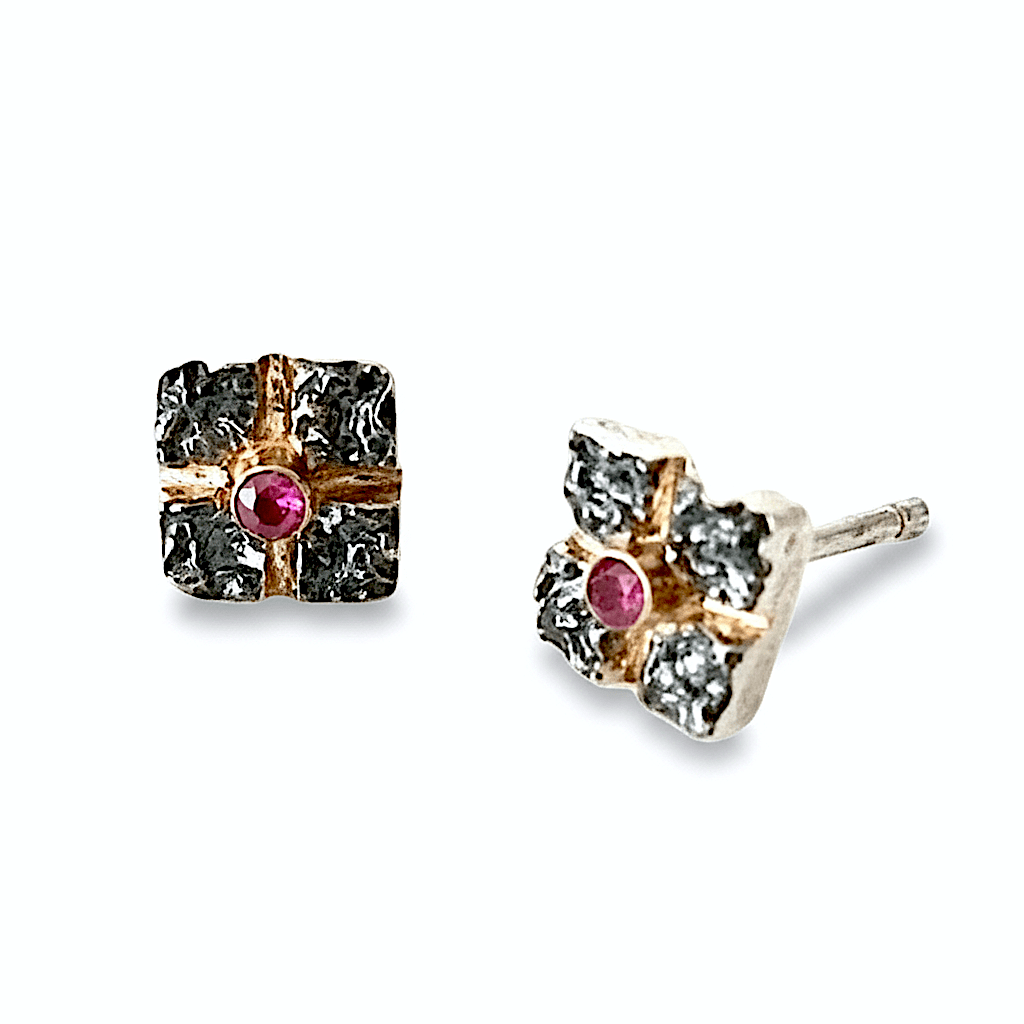 Clous d'oreilles carrés en argent texturé, et oxydé entrecroisés par 2 lignes or jaune, au centre un rubis. Un bijou moderne et élégant fait à la main par l'artisan joaillier Apostolos kleitsiotis Grec.