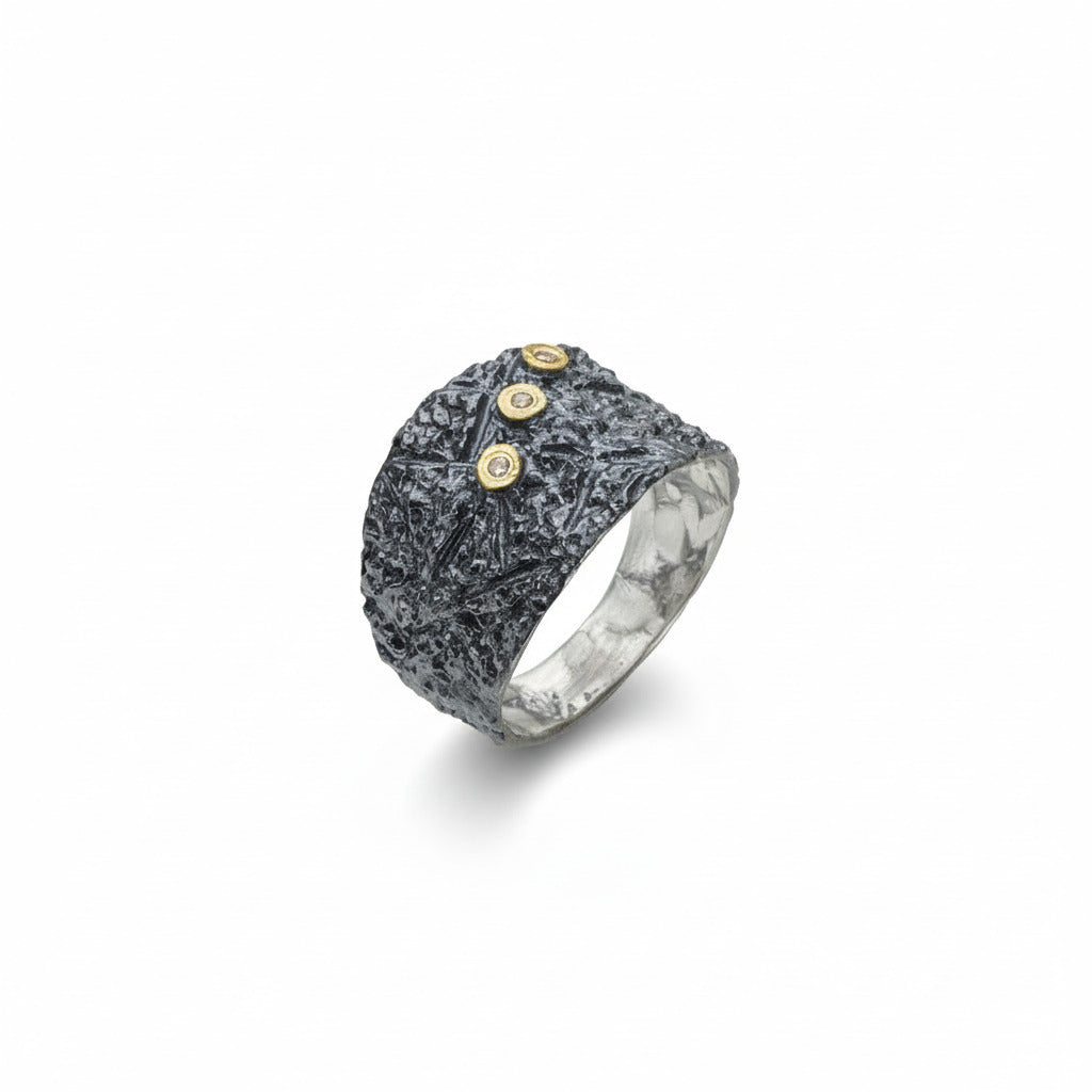 Cette bague en argent patiné et texturé se distingue par trois diamants taille brillant, sertis en or jaune sur dessus, alignés de côté.