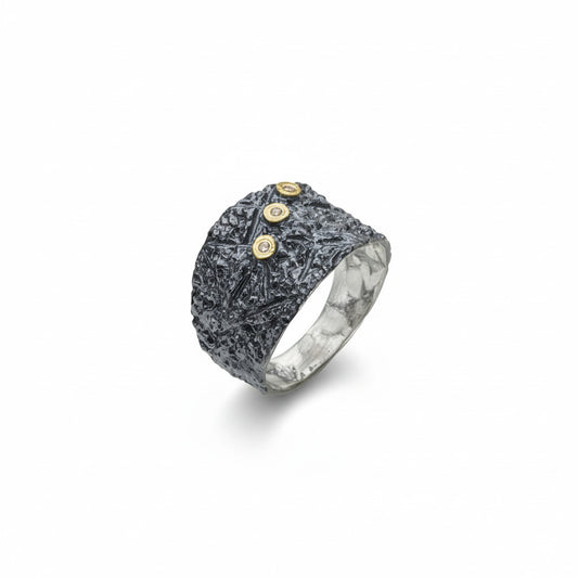 Cette bague en argent patiné et texturé se distingue par trois diamants taille brillant, sertis en or jaune sur dessus, alignés de côté.