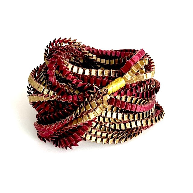 Long sautoir de couleur olive et bordeaux composé de huit bandes de satin plissé reliées les unes aux autres par un lien de coton jaune.