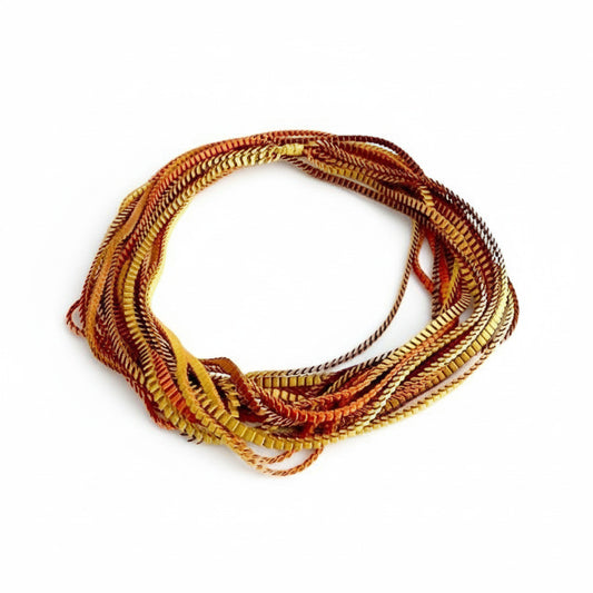 Sautoir de couleur marron, doré, cuivré composé de huit bandes de trois millimètres de satin plissé reliées les unes aux autres par un lien de coton jaune d'or. À porter ong ou en double selon l'humeur.