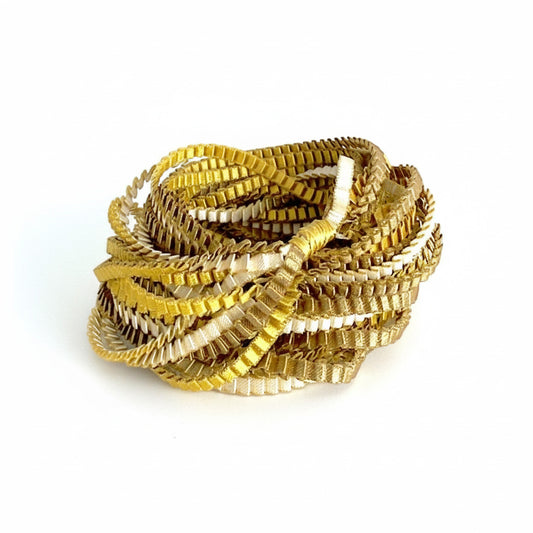 Long sautoir de couleur kaki, ivoire et doré composé de huit bandes de trois millimètres de satin plissé reliées les unes aux autres par un lien de coton jaune d'or.