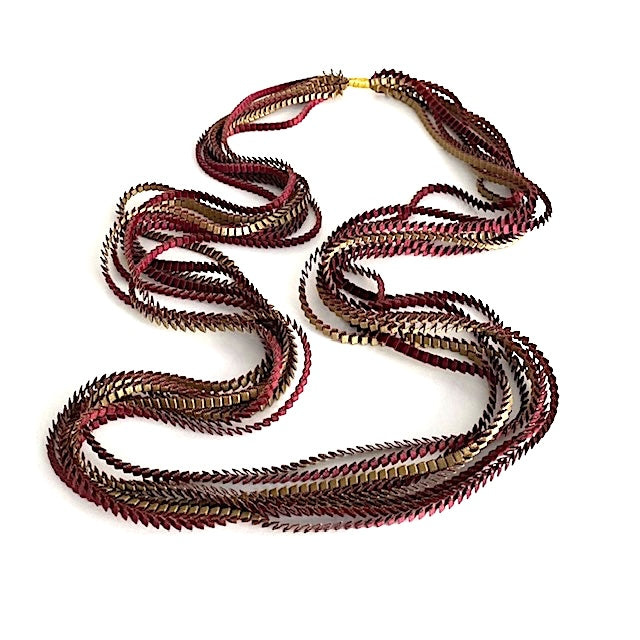 Long sautoir de couleur bordeaux et olive composé de huit bandes de satin plissé reliées les unes aux autres par un lien de coton jaune. 