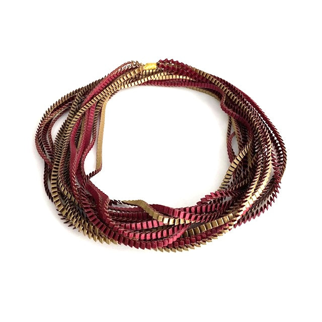 Long sautoir de couleur olive et bordeaux composé de huit bandes de satin plissé reliées les unes aux autres par un lien de coton jaune. peut-être porté en double.