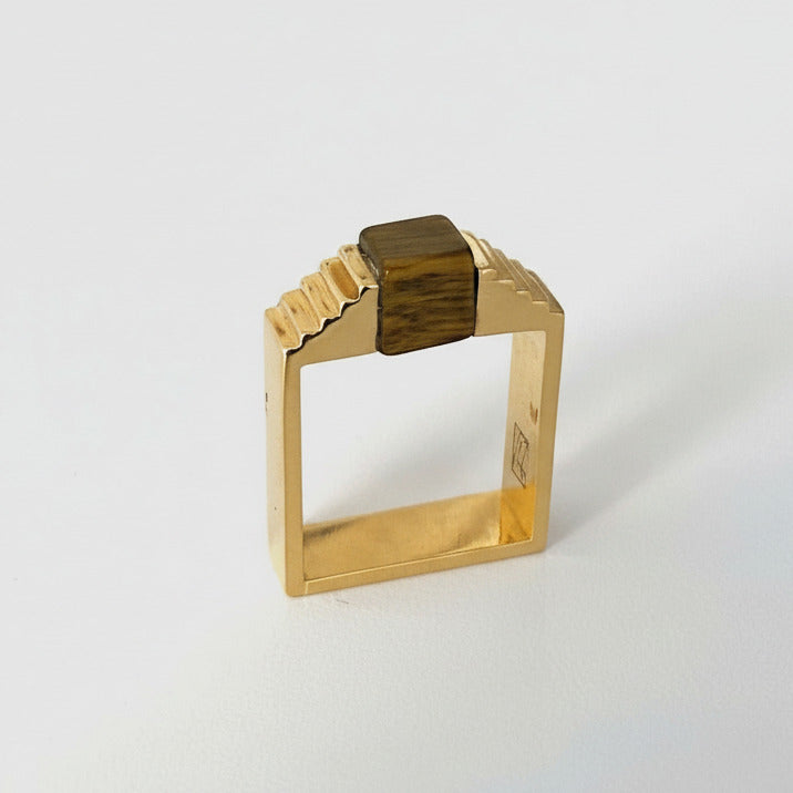 Bague géométrique en vermeil avec une pierre oeil de tigre en forme de cube, imbriqué entre deux éléments en formes d'escalier.