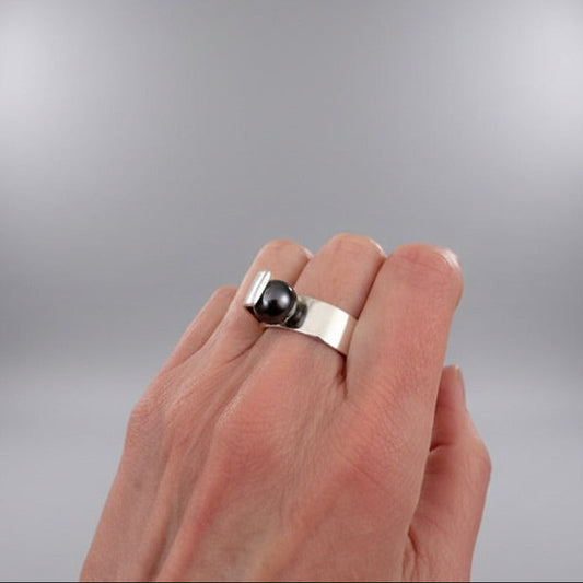 Bague S en argent avec perle noire de Tahiti. Design ouvert, ligne minimaliste et finition poli miroir. Bijou porté.