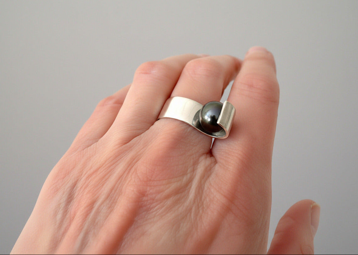 Bague au design minimaliste en argent et perle noire, détail du bijou porté.