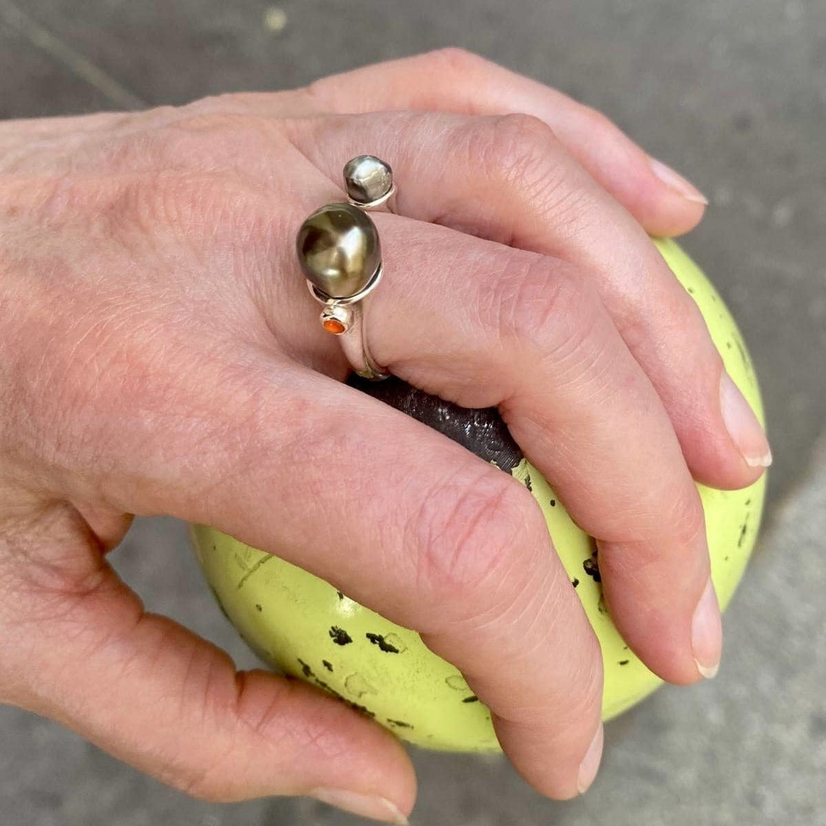 Bague ouverte en argent avec d'un côté une perle keishi et de l'autre une perle tahitienne au reflet vert ornée d'une opale orange du Mexique. 