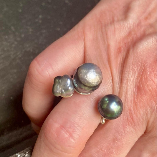 Bague ouverte présentant deux perles de Tahiti  sculptée,de couleurs différentes. L'anneau en argent est orné de petites pierres de couleurs.