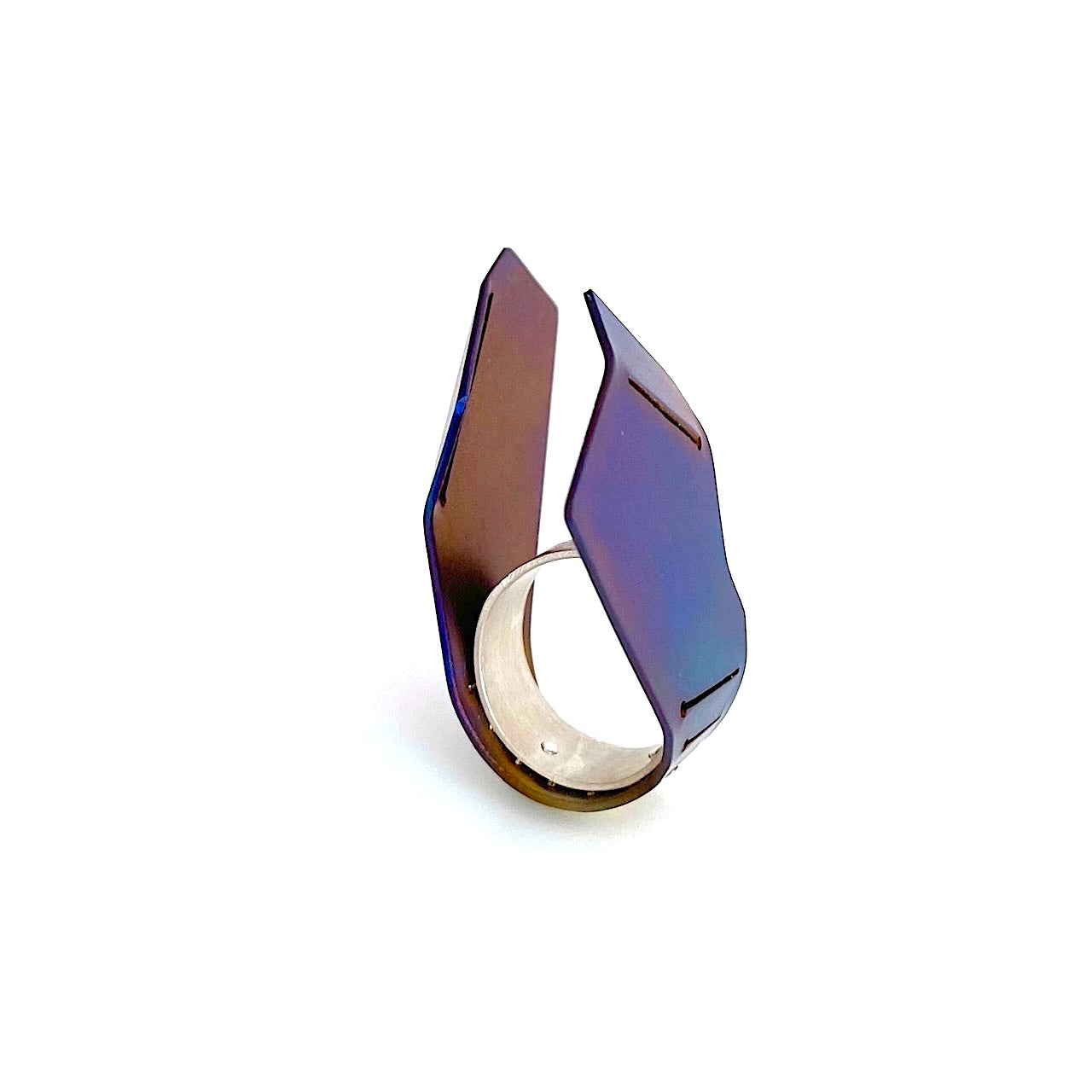 Cette bague asymétrique, toute en hateur aux formes aériennes est construite comme deux ailes verticales,  à partir d'une plaque de titane pliée, sciée, et rivetée à un anneau d'argent. La surface du métal est chauffé à la flamme pour un rendu bleu vif aux nuances brun, violet.