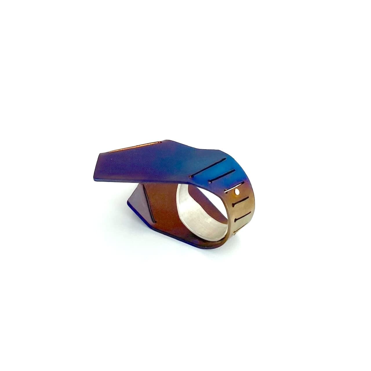 Cette bague asymétrique aux formes aériennes est construite comme deux ailes verticales,  à partir d'une plaque de titane pliée, sciée, puis rivetée à un anneau d'argent. La surface du métal est chauffé à la flamme pour un rendu bleu vif aux nuances brun, violet.