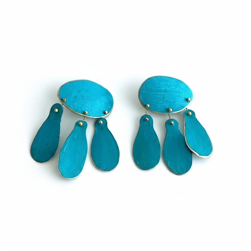 Cette paire de boucles d'oreilles réinterprète les bijoux du XIIIe siècle, en bronze laminé, composée d’un ovale et de trois pampilles allongées, elle allie lignes historiques et design minimaliste. Elles sont peintes à la main avec des pigments acryliques bleu turquoise.