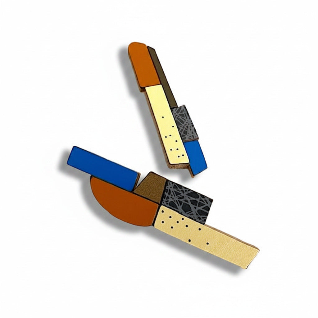 Des boucles d’oreilles longues et asymétriques associant des éléments géométriques en bois et formica. Ces pièces uniques, réalisées à la main par l’artiste belge Karen, mêlent des couleurs multiples : bleu foncé, marron chaud, jaune pâle, bronze métallisé, aux finitions mates ou avec motifs texturés.