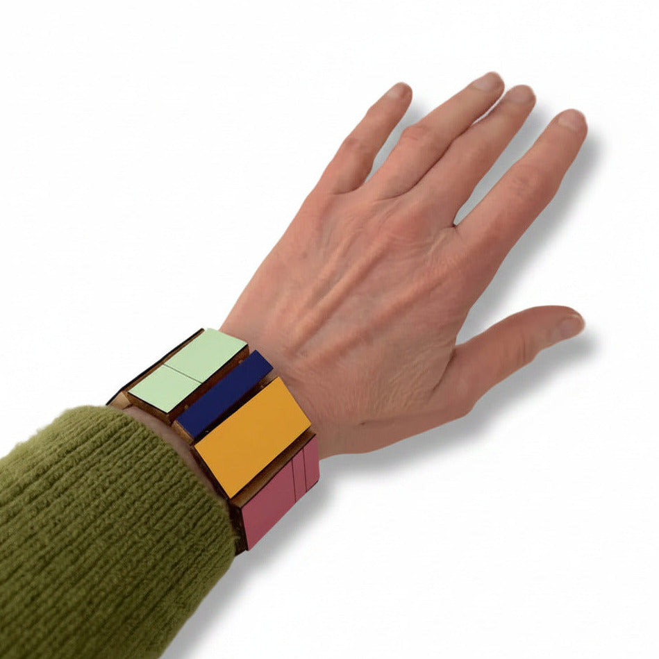 Ce bracelet géométrique articulé en bois et Formica multicolore se compose de 11 rectangles de tailles variées, assemblés dans une composition graphique. Il est doté d’un fermoir crochet en argent patiné noir. Bijou porté.