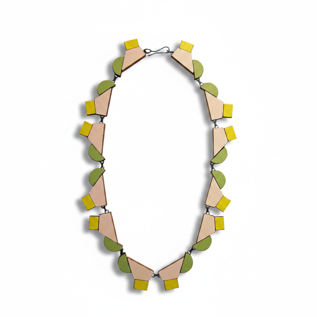 Ce collier design réunit 12 éléments géométriques en bois et formica rose poudré, vert, pastel et  jaune clair reliés par des attaches en argent patiné noir et fermés par un fermoir crochet. Bijou contemporain fait à la main par l'artste belge Karen Vanmol.