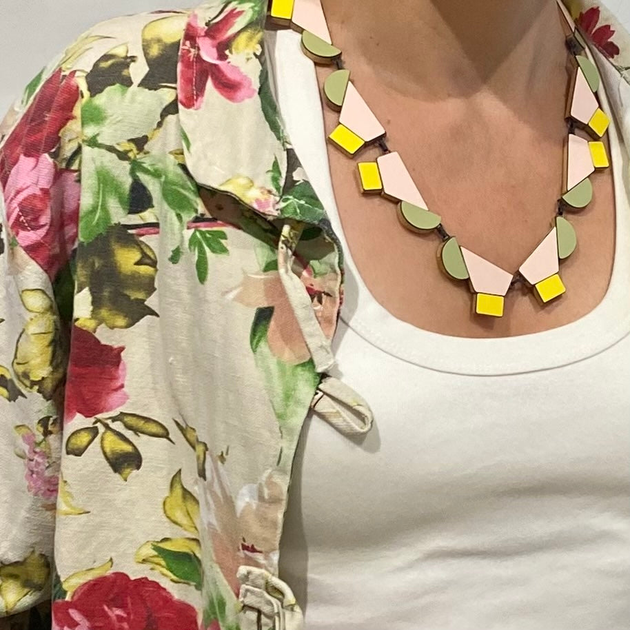 Ce collier design réunit 12 éléments géométriques en bois et formica rose poudré, vert, pastel et  jaune clair reliés par des attaches en argent patiné noir et fermés par un fermoir crochet. Bijou contemporain fait à la main par l'artiste belge Karen Vanmol. Joyeux et moderne, il s'adapte à toutes les encolures.