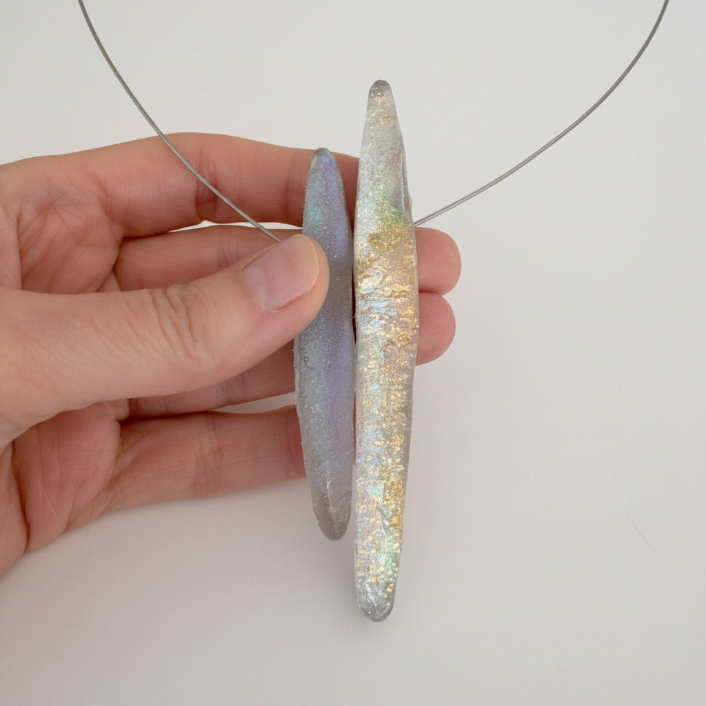 Détail collier graphique en résine opalescente grise sur câble fin. Bijou contemporain artisanal aux reflets subtils, fabrication française et artisanale.