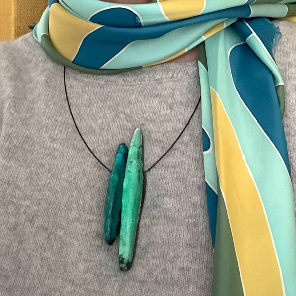 Détail, collier contemporain deux éléments allongés en résine texturée, dans des nuances de vert émeraude et céladon. Bijou porté.