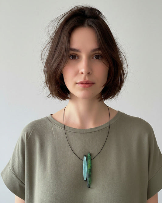 Collier design vert et bleu inspiré de la nature. Il e compose de deux éléments en résine irisée, un bleu claire et un vert présentés sur un câble noir fin. Vue portée du collier contemporain.