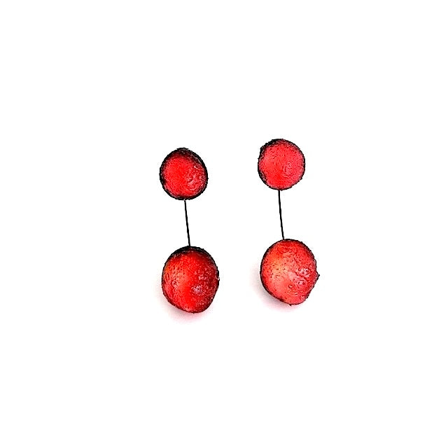  Boucles pendantes composées de deux sphères en résine texturée rouge, reliées par un câble fin et solide, noir. Pour oreilles percées.