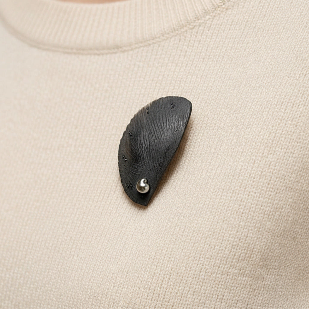 Broche contemporaine en corne brune sculptée et texturée, ornée d'une perle de Tahiti. Bijou en  forme de demi cercle porté sur un pull.