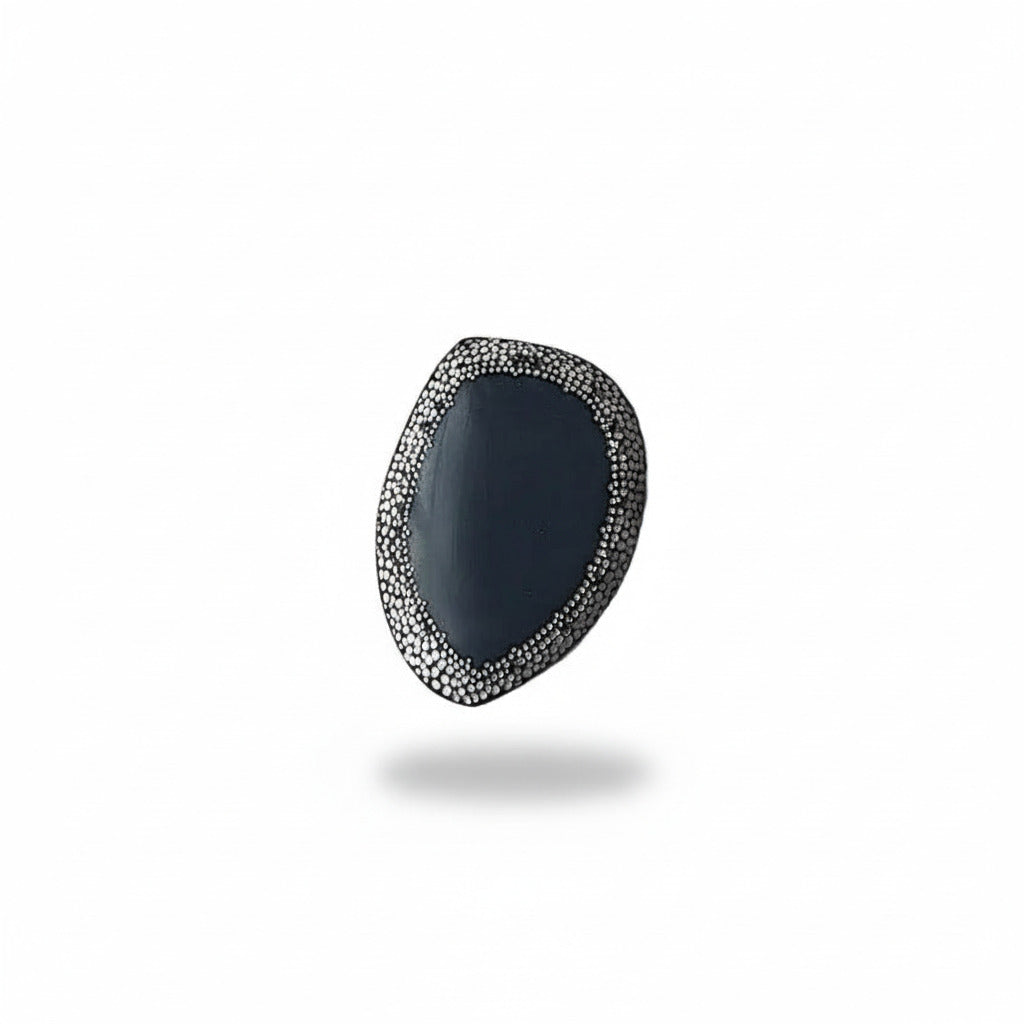 Broche unique en corne noire ornée d'une frise de 50 mm composée de points blancs peints à la main, rappelant le pointillisme de l'art aborigène. De mini perles d'hématites soulignent ce travail abstrait. 