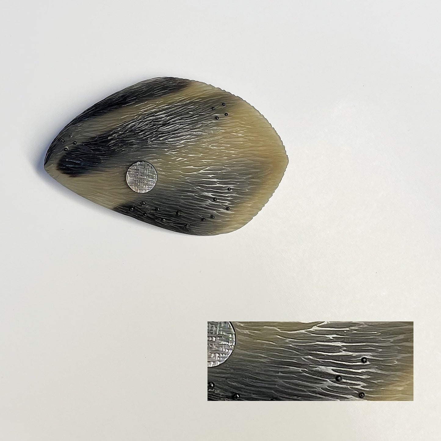 broche ovale, sculptée en corne dorée aux dessins bruns naturels. Le bijou est gravé, orné d'une pastille de nacre grise  et de fil de nylon perlé. Une pièce contemporaine réalisée à la main en pièce unique.