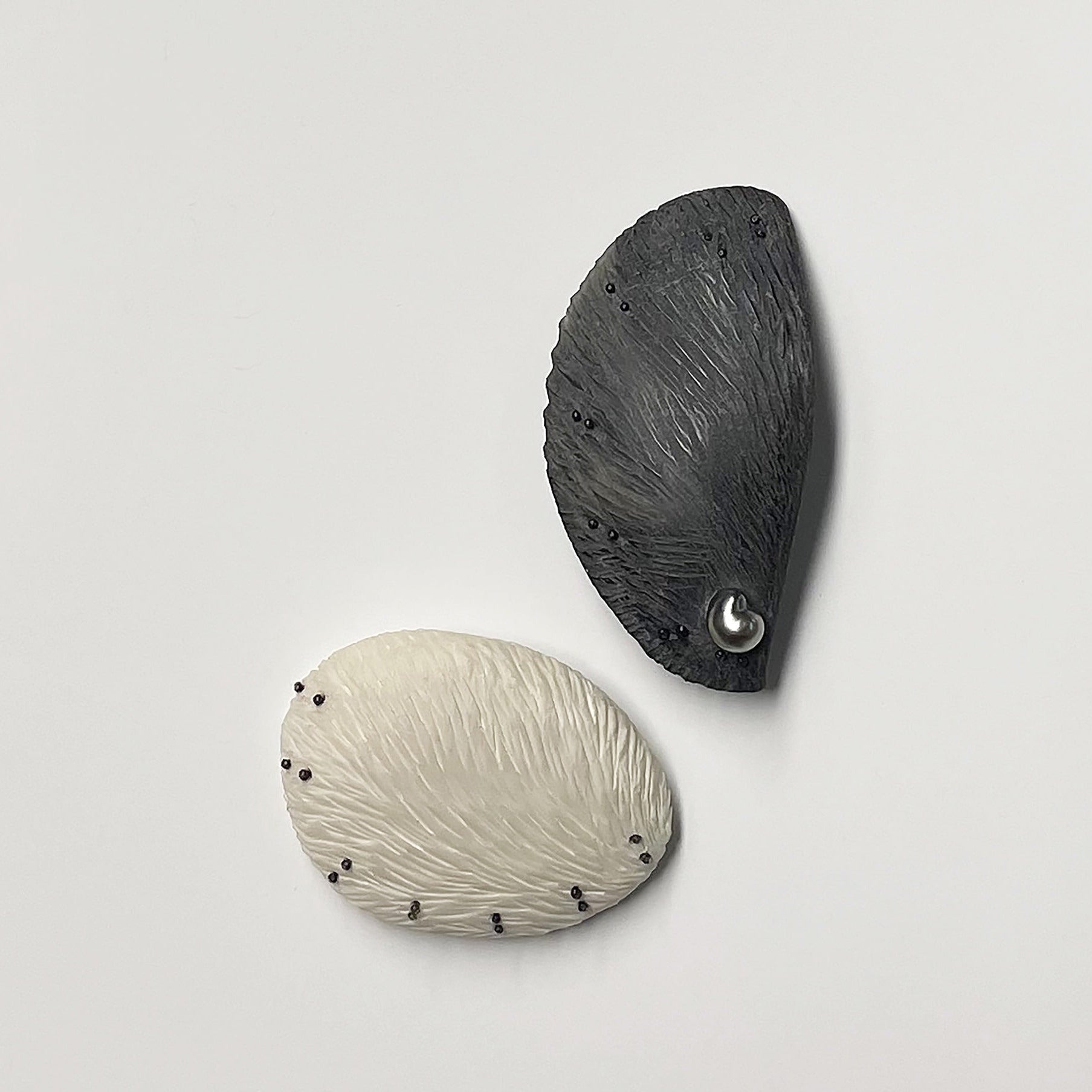 Deux broches contemporaines sculptées à la main et réalisées en pièces uniques par la créatrice Marie Pierre Ginestet. L'une est en corne brune et perle tahitienne et l'autre en os gravé.
