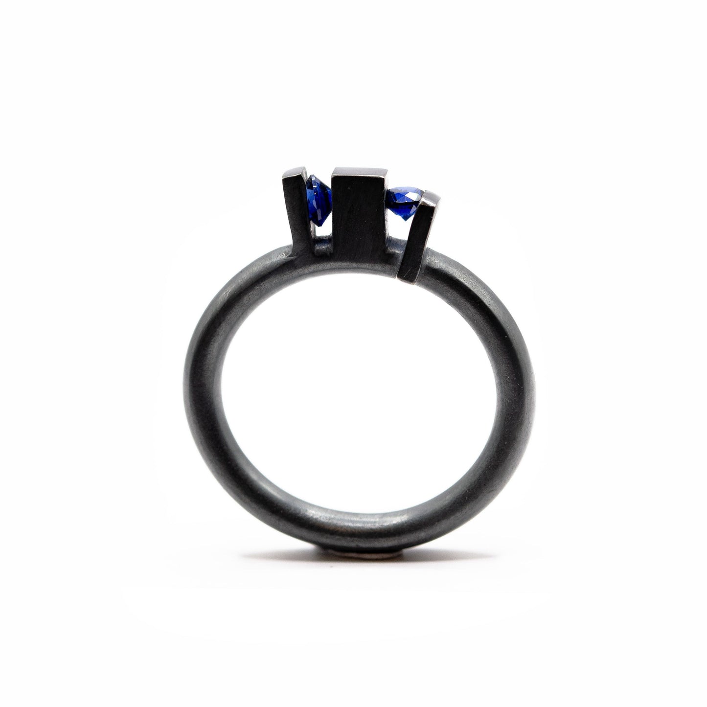 Bague contemporaine en argent forgé et oxydé avec anneau rond et volumes verticaux sculpturaux, sertie de deux saphirs de culture bleus.