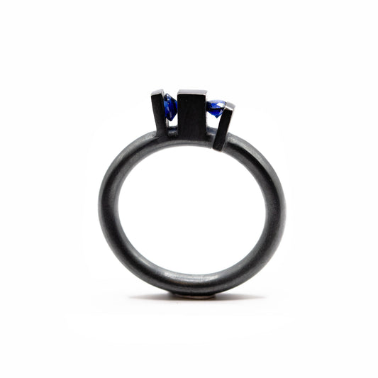 Bague contemporaine en argent forgé et oxydé avec anneau rond et volumes verticaux sculpturaux, sertie de deux saphirs de culture bleus.