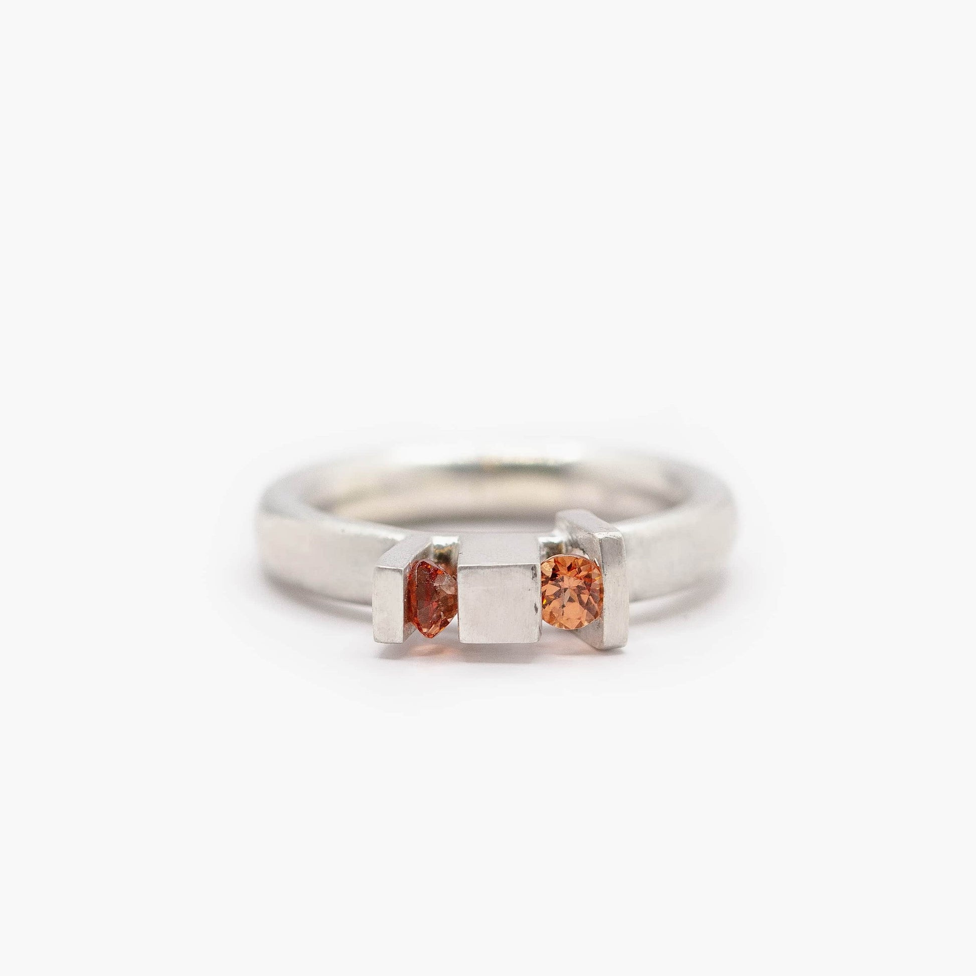 Bague épurée en argent avec anneau rond et volumes architecturaux, sertie de deux grenats spessartite aux teintes orange lumineuses. fabrication artisanale.