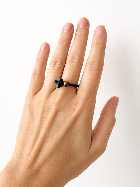 La bague Offshoots s'inspire de la manière dont les plantes se développent. En argent oxydé, elle est sertie d'une perle noire aux reflets mordoré et d'un grenat rouge lumineux. Bijou porté au majeure.
