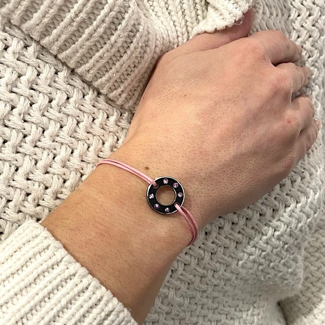 Bracelet Ready-Made petit modèle signé Charlotte Romer, rondelle en aluminium anodisé noir sertie de six saphirs roses. Bijou upcyclé présenté sur un lien réglable en coton ciré rose. Bijou porté.