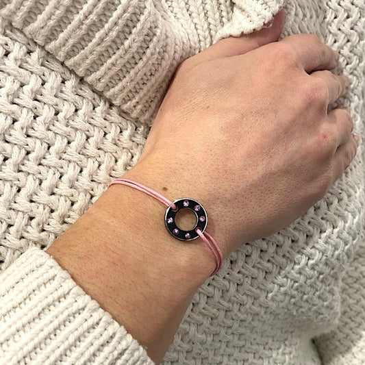 Bracelet Ready-Made petit modèle signé Charlotte Romer, rondelle en aluminium anodisé noir sertie de six saphirs roses. Bijou upcyclé présenté sur un lien réglable en coton ciré rose. Bijou porté.