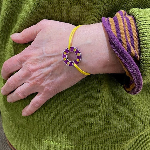 Bracelet Ready-Made composé d'une rondelle en aluminium violet sertie de  six saphirs jaunes facettés. Bracelet design et unisexe présenté sur lien de coton ciré. Bijou porté. 