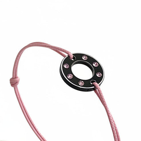 Bracelet Ready-Made petit modèle signé Charlotte Romer, rondelle en aluminium anodisé noir sertie de six saphirs roses. Bijou upcyclé présenté sur un lien réglable en coton ciré rose.