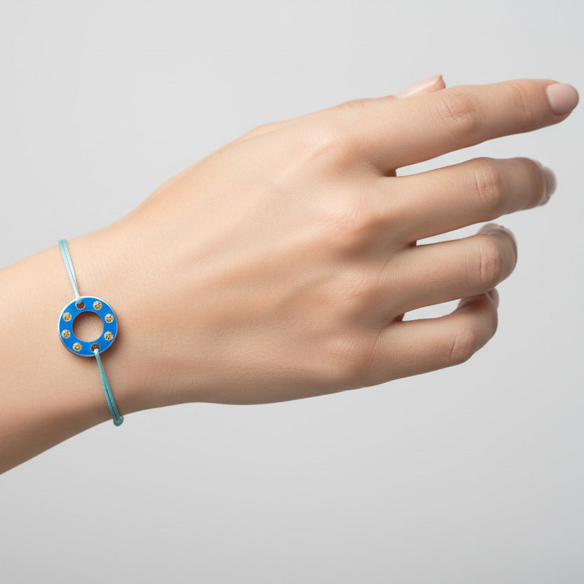 Bracelet Ready-Made petit modèle signé Charlotte Romer, rondelle en aluminium anodisé bleu sertie de six saphirs jaunes. Bijou upcyclé présenté sur un lien réglable en coton ciré. 