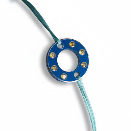 Bracelet Ready-Made petit modèle signé Charlotte Romer, rondelle en aluminium anodisé bleu sertie de six saphirs jaunes. Bijou upcyclé présenté sur un lien réglable en coton ciré. 