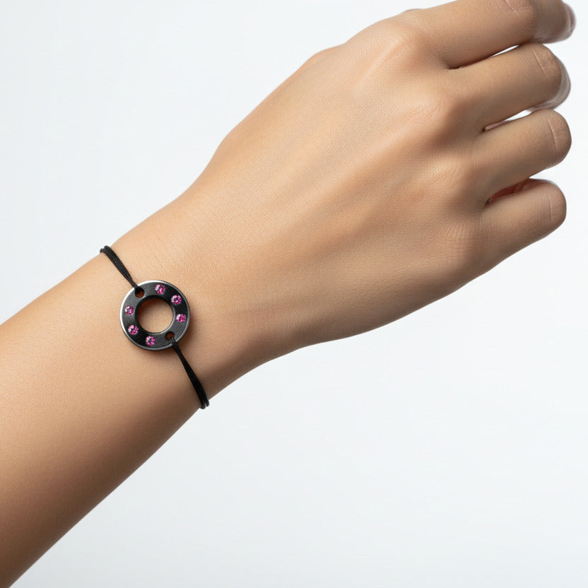 Bracelet Ready-Made petit modèle signé Charlotte Romer, rondelle en aluminium anodisé noir sertie de six saphirs roses. Bijou upcyclé présenté sur un lien réglable en coton ciré. Bijou porté.