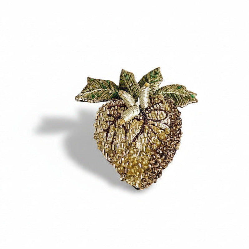 Broche sculpturale en textile brodée main en forme de cœur, ornée de mini perles de verre et de sequins dans des tons de de doré, vert et kaki. Détails : quatre feuilles sur le haut du cœur et nervures brodées soulignent l'inspiration nature de cette broche contemporaine.