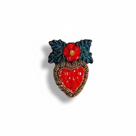 La petite broche Cœur de houx évoque un cœur d’or couronné de feuillage et d'une fleur. Ornée de perles de verre rouges et d’un feuillage brodé vert, cette pièce délicate révèle un travail minutieux de broderie main à l’aiguille. Création artisanale signée Trovelore.