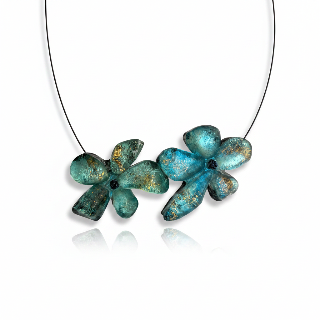Collier en résine bleu vert avec reflets irisés, et détail pailleté à la feuille d'or, présenté sur cable acier noir. Fermoir aimanté à l'avant inséré dans les fleurs. Bijou floral fait main.