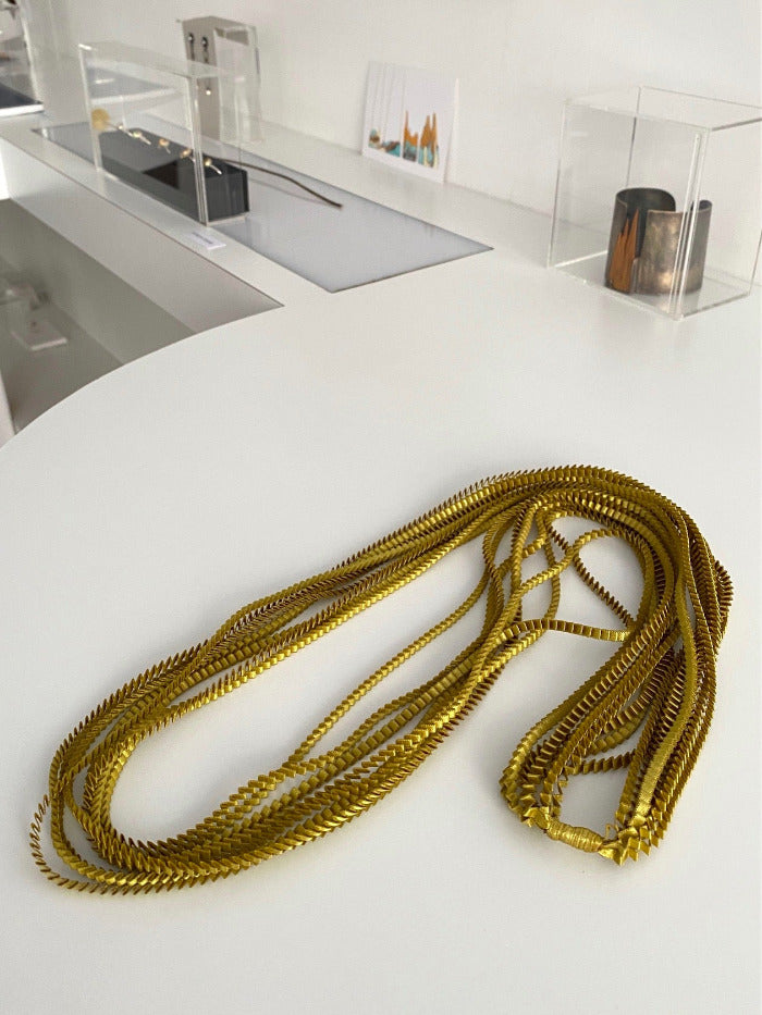 Long collier coloré composé de huit bandes de satin plissé gold reliées les unes aux autres par un lien de coton jaune 
