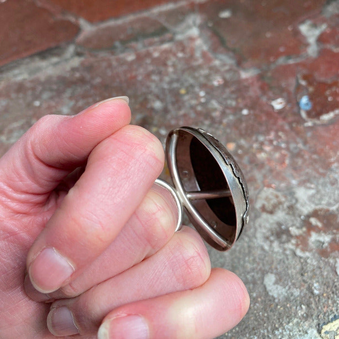 Bague en forme de dôme en fer rouillé avec structure argent présentée sur main de femme, décor briques 
